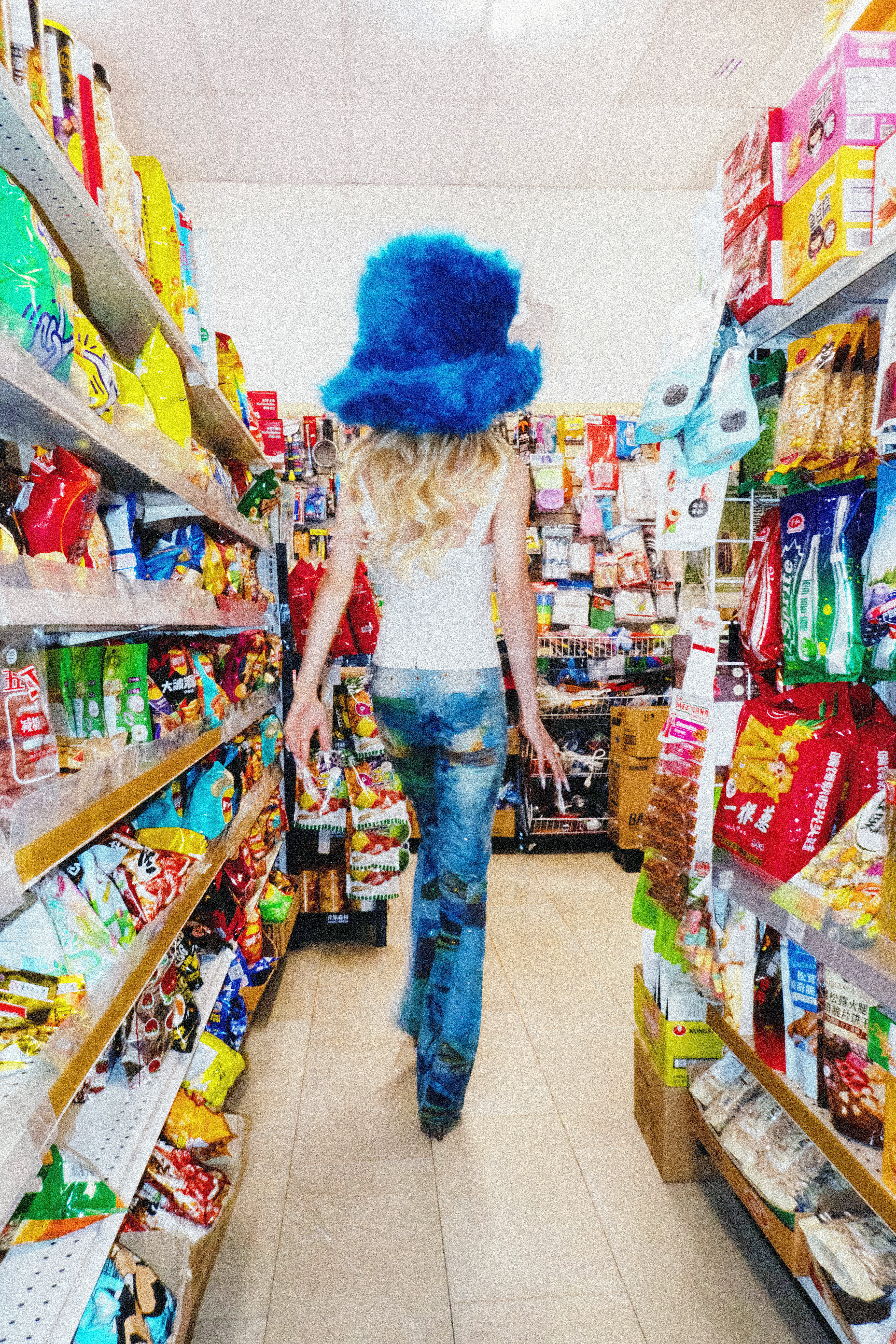 Jesse in Y2K inspired drag walking away with their back to the camera in a colorful conveinence store